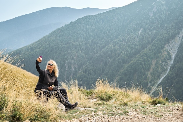 An adult woman takes a selfie at a rest stop during a hike in the mountains active recreation