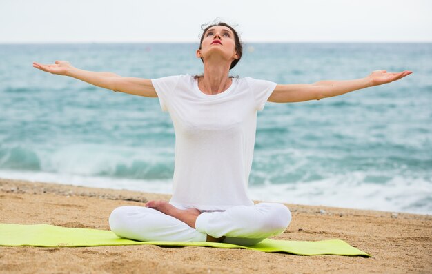 Adult woman in white T-shirt is sitting and practicing asana