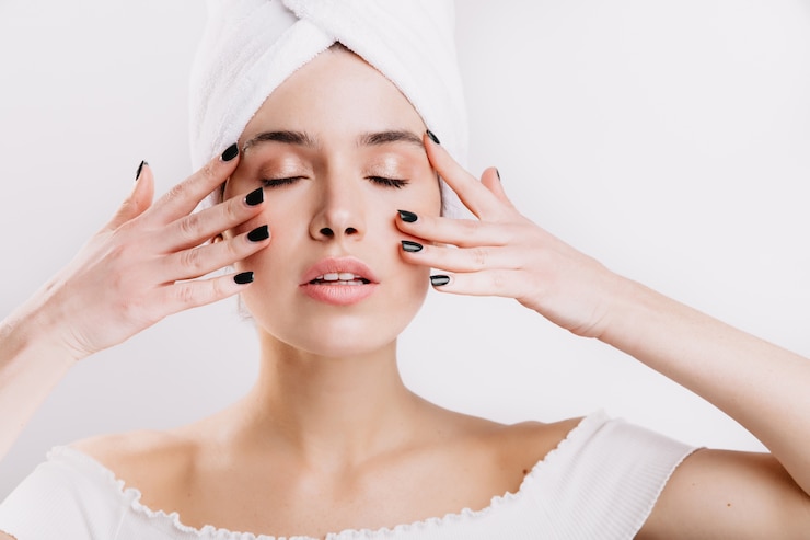Free Photo adult woman with healthy skin massages her face to prolong youth. snapshot of girl after shower on isolated wall.