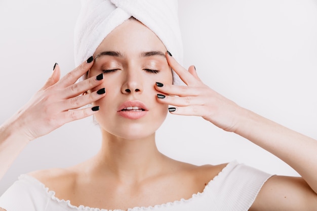 Adult woman with healthy skin massages her face to prolong youth. Snapshot of girl after shower on isolated wall.