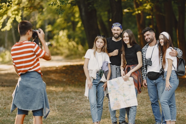 Concetto di avventura, escursione e persone. gruppo di amici sorridenti in una foresta. guy scatta una foto.