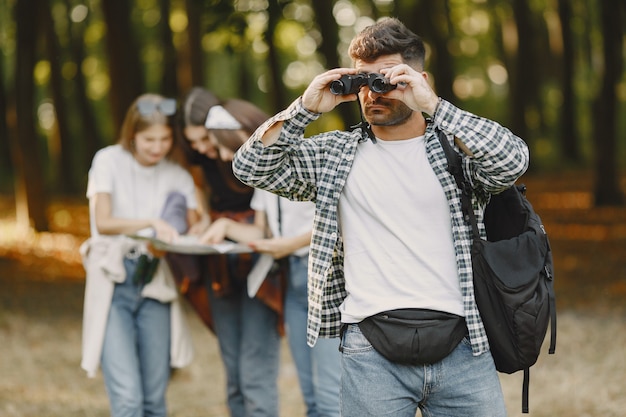 Adventure, hike and people concept. Group of smiling friends in a forest. Man with binocular.
