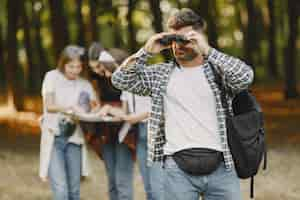 Foto gratuita concetto di avventura, escursione e persone. gruppo di amici sorridenti in una foresta. uomo con il binocolo.