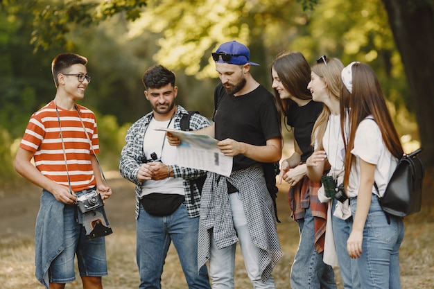 Adventure, hike and people concept. Group of smiling friends in a forest. Man with a map.