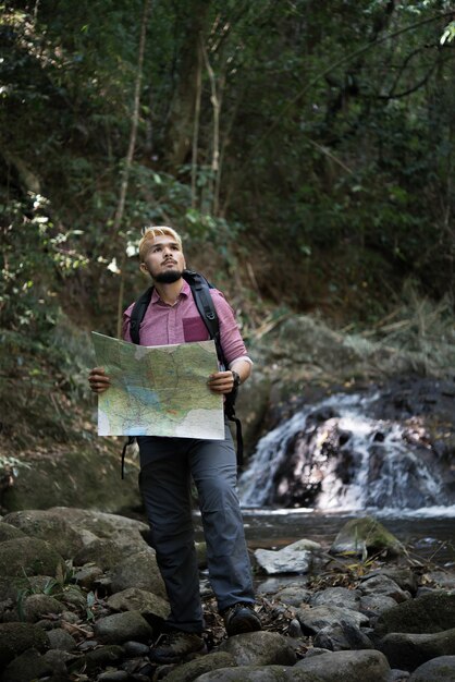 冒険の男は正しい道を見つけるために山道の地図を観察します。