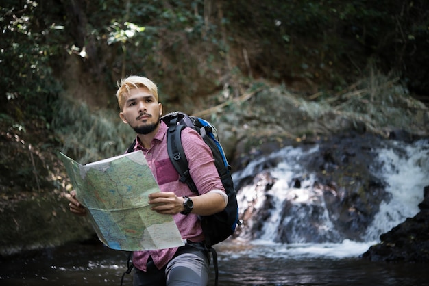 冒険の男は正しい道を見つけるために山道の地図を観察します。