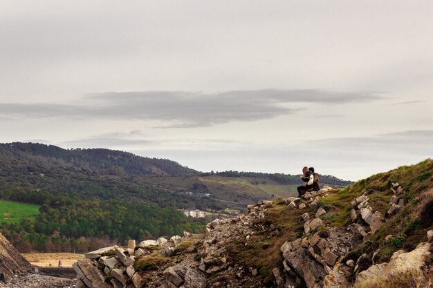 Adventurous romantic hiker couple sitting on the rocks and looking at the mountains