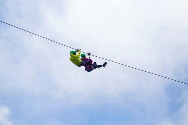 Adventurous tourist zip lining against cloudy sky