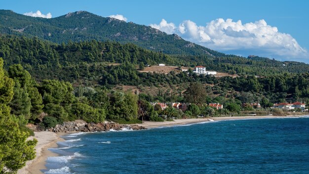 Aegean sea coast of Greece, rocky hills with growing trees and bushes, buildings located near the coast