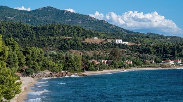 Aegean sea coast of Greece, rocky hills with growing trees and bushes, buildings located near the coast