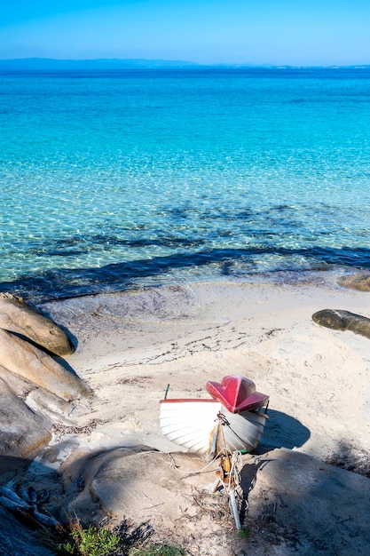 Aegean sea coast with beached boat, rocks on the beach, blue water, Greece