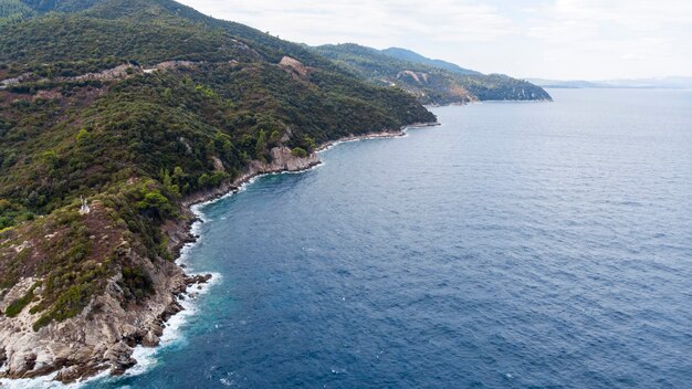 Aegean sea coast with blue transparent water, greenery around, rocks, bushes and trees, view from the drone Greece