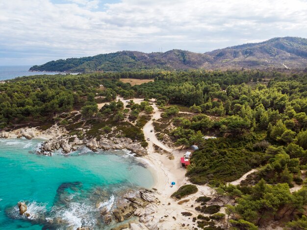 青い透明な水、周りの緑、岩、茂みや木々、ドローンからの眺め、ギリシャのエーゲ海の海岸