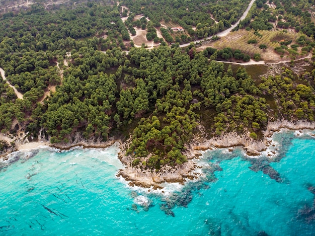 青い透明な水、周りの緑、岩、茂みや木々、ドローンからの眺め、ギリシャのエーゲ海の海岸