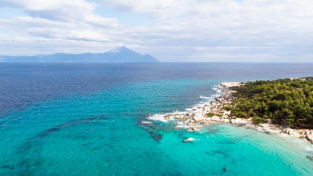 푸른 투명한 물, 주변의 녹지, 바위, 관목 및 나무가있는에게 해 해안, 무인 항공기, 그리스에서보기