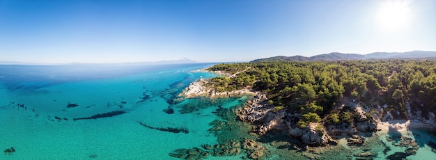 Aegean sea coast with blue transparent water, greenery around, rocks, bushes and trees, view from the drone, Greece