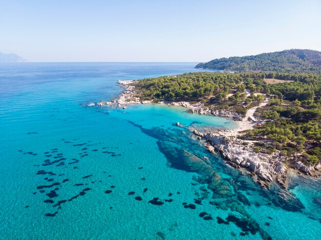푸른 투명한 물, 주변의 녹지, 바위, 관목 및 나무가있는에게 해 해안, 무인 항공기, 그리스에서보기