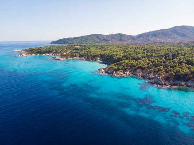 青い透明な水、周りの緑、岩、茂みや木々、ドローンからの眺め、ギリシャのエーゲ海の海岸