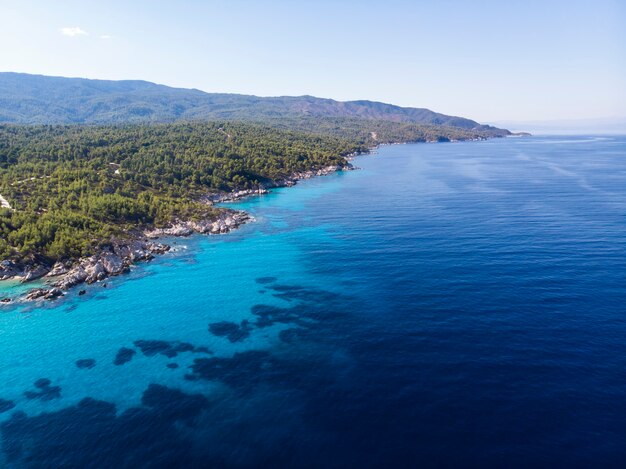 Побережье Эгейского моря с голубой прозрачной водой, зелень вокруг, вид с дрона, Греция