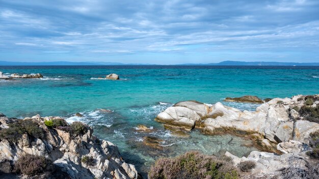 周りに緑、岩や茂み、波のある青い水、ギリシャのエーゲ海の海岸