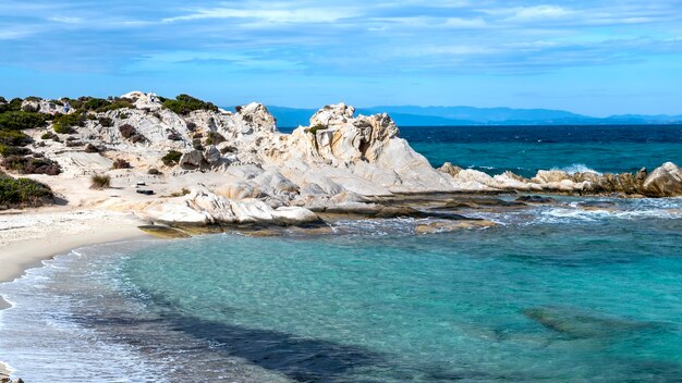 Побережье Эгейского моря с зеленью вокруг, скалами и кустами, голубая вода с волнами, Греция