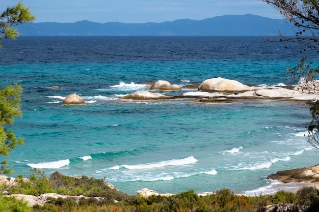 Costa del mar egeo con vegetazione intorno, rocce e alberi, acqua blu con onde, grecia