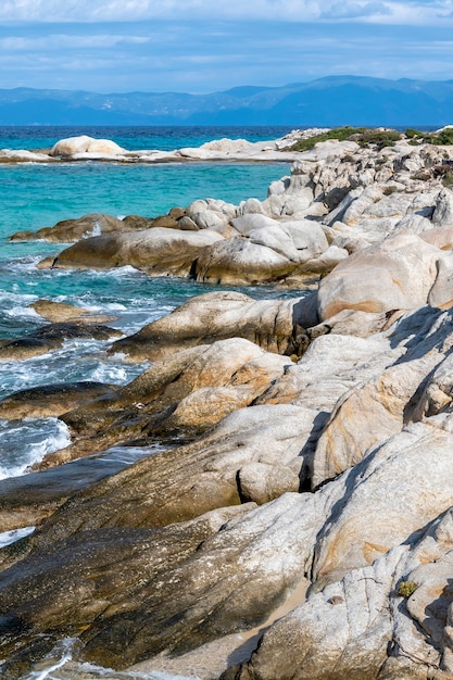 Aegean sea coast with rocks, bushes and land, blue water with waves, Greece