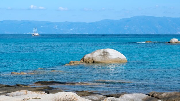 Aegean sea coast with rocks over the water, boat and land, blue water, Greece