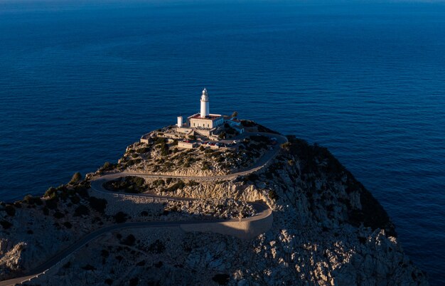 Aerial distant shot of a high rocky cliff with a white tower built on top in the middle of the ocean