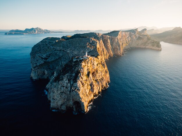 Aerial distant shot of a high rocky cliff with a white tower built on top in the middle of the ocean