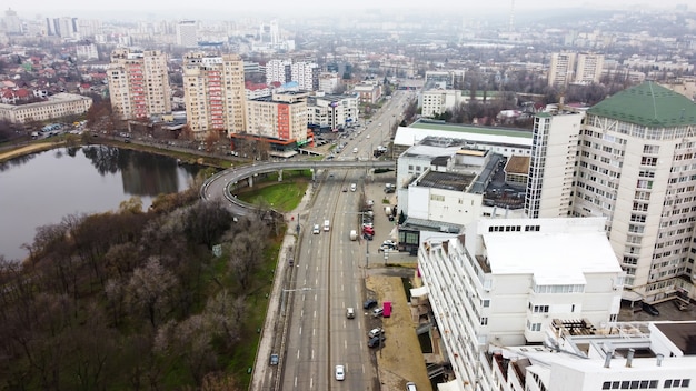 Aerial drone panorama view of Chisinau, street with multiple residential and commercial buildings, road with moving cars, lake with bare trees