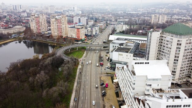 Aerial drone panorama view of Chisinau, street with multiple residential and commercial buildings, road with moving cars, lake with bare trees