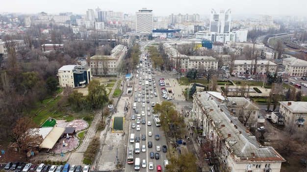 Aerial drone panorama view of Chisinau, street with multiple residential and commercial buildings, road with multiple moving cars, park with bare trees