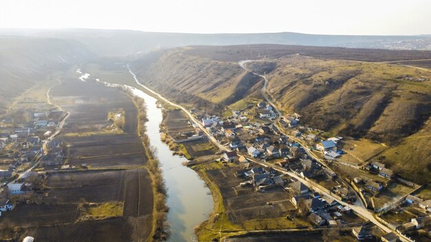 Aerial drone panorama view of a village located near a river and hills, fields, fog in the air, Moldova