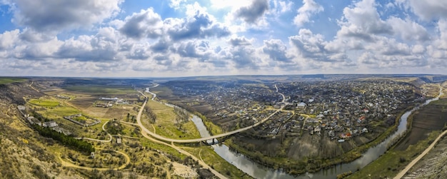 Панорама с воздуха с дрона на деревню, расположенную рядом с рекой и холмами, полями, солнечными лучами, облаками в Молдове