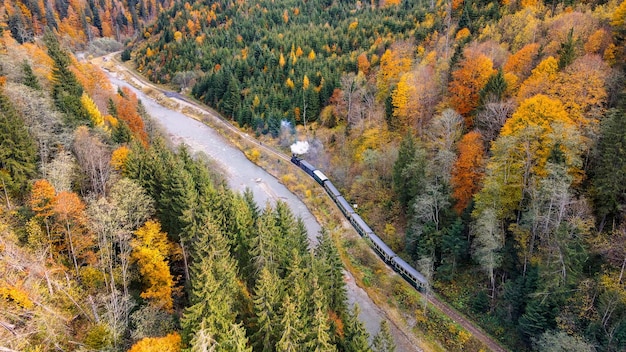 Aerial drone view of the moving steam train Mocanita in a valley along a river hills covered