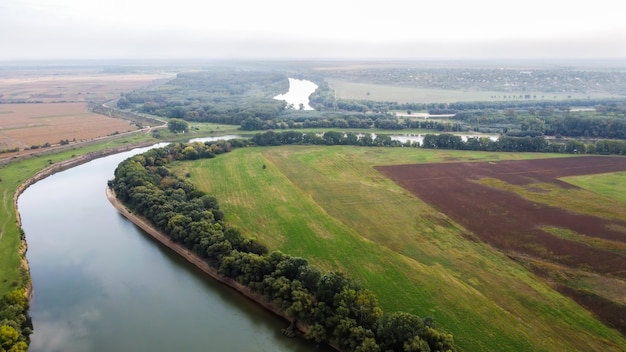 Aerial drone view of nature in Moldova, floating river with reflecting sky, green fields with trees, fog in the air