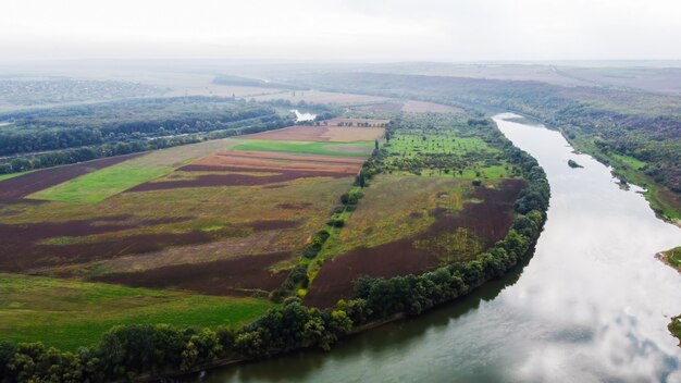 Aerial drone view of nature in Moldova, floating river with reflecting sky, green fields with trees, fog in the air