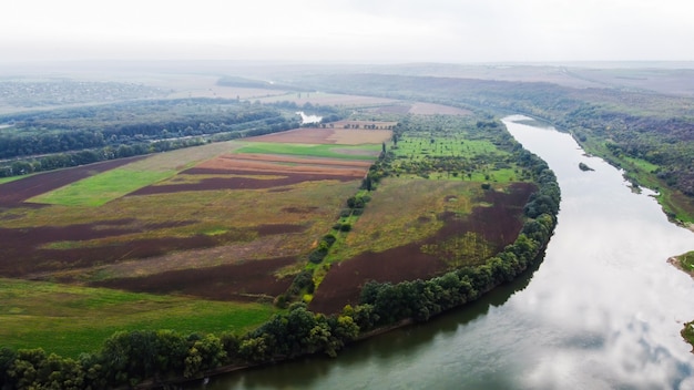 Aerial drone view of nature in Moldova, floating river with reflecting sky, green fields with trees, fog in the air