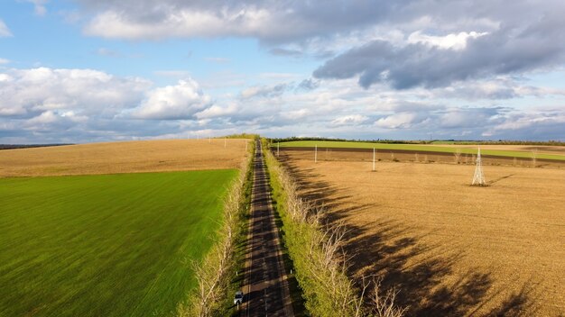 Aerial drone view of nature in Moldova, sown fields, road with moving car, trees along it, cloudy sky
