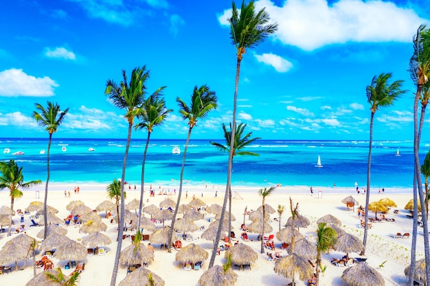 짚으로 만든 우산, 야자수, 보트가 있는 아름다운 카리브해 열대 해변의 공중 무인 항공기 보기. 바바로, 푼타 카나, 도미니카 공화국. 휴가 배경. 프리미엄 사진