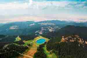 Foto gratuita vista aerea del drone del lago poiana brasov romania situato sulla cima della montagna ricoperta da una lussureggiante città forestale in lontananza