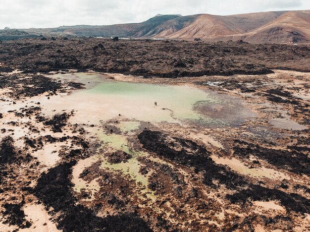 Aerial shot of a beautiful muddy tarn lake with two people walking in it