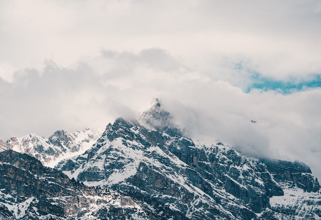 Aerial shot of beautiful rocky snowy mountains covered in clouds