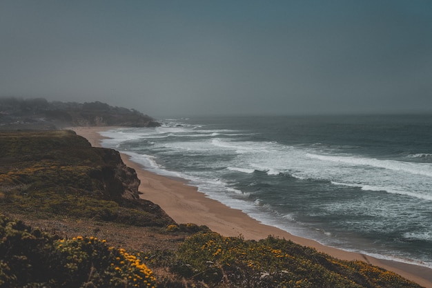 Aerial shot of the beautiful sandy coast of the sea with a dark grey sky