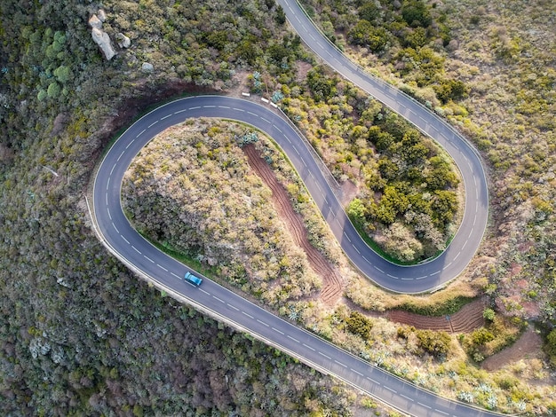 Aerial shot of a car passing through a spiral road surrounded by trees in the countryside