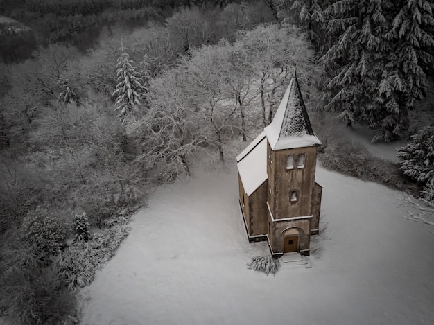 Aerial shot of a church covered in the snow surrounded by leafless trees