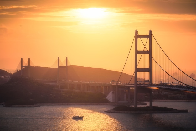 Aerial shot of city buildings, hills, and a bridge over a river at sunset