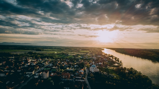 Aerial shot of a city near a river and grassy fields under a cloudy sky