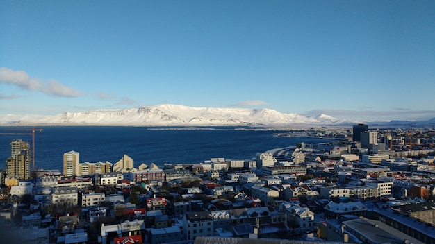 青い空を背景に雪に覆われた山々とレイキャビクの沿岸都市の空中ショット